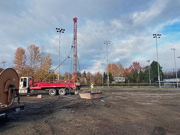 a tall drill machine with a person in a hard hat stands in a muddy field