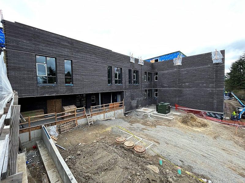 the corner of a dark brick 2 story building with windows forms an L shape with construction materials on the ground