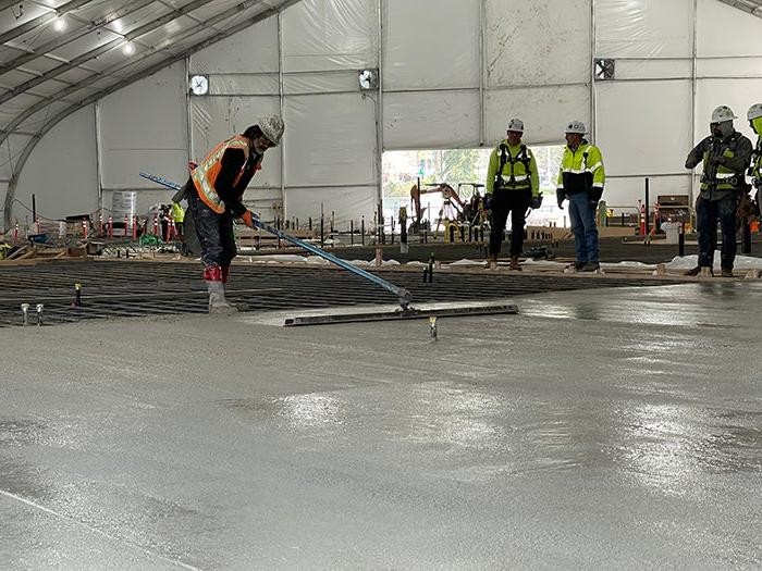 a worker in a safety vest and hardhat is smoothing concrete in a large flat area