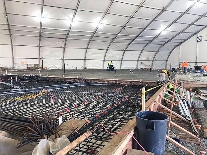 a grid of rebar inside concrete frames under a large tent