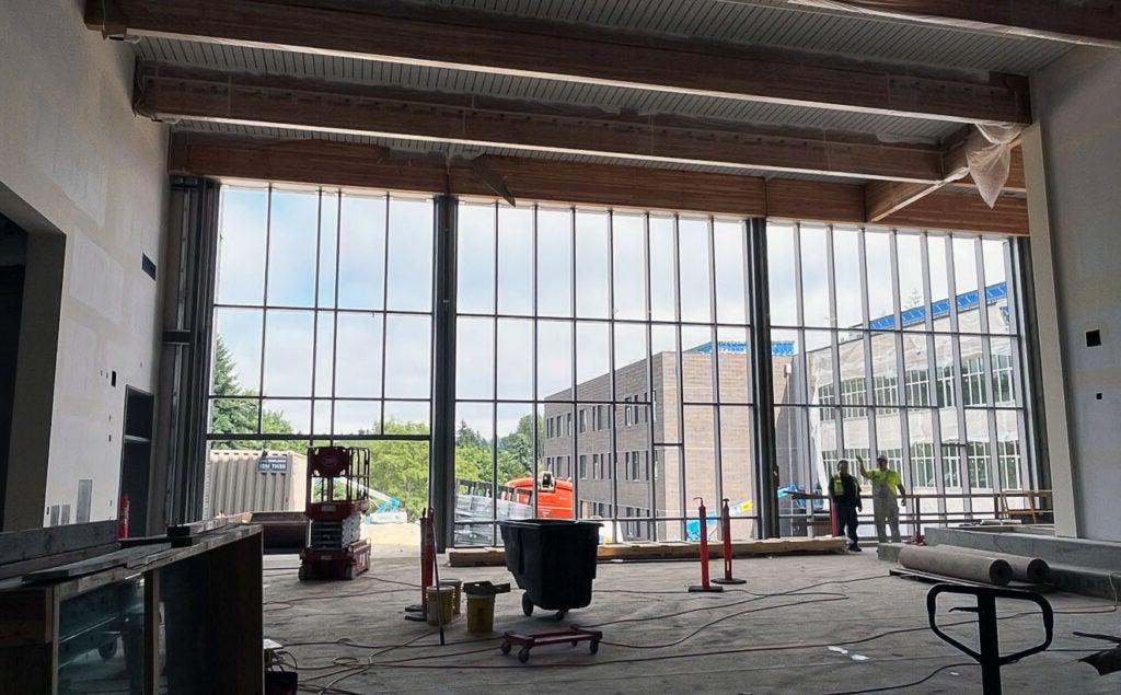 a two-story glass window wall is being installed. construction equipment can be seen and a large brick building is outside the window