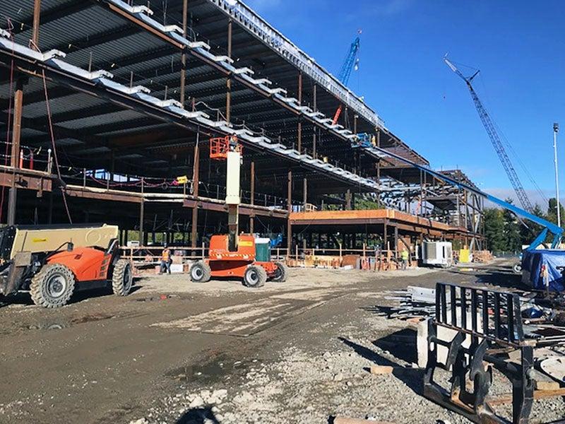 a four story steel frame for a large building with construction cranes, lifts, and other machines