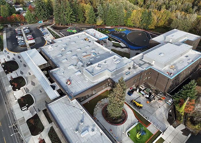 aeriel of a large building with a white roof with trees behind it