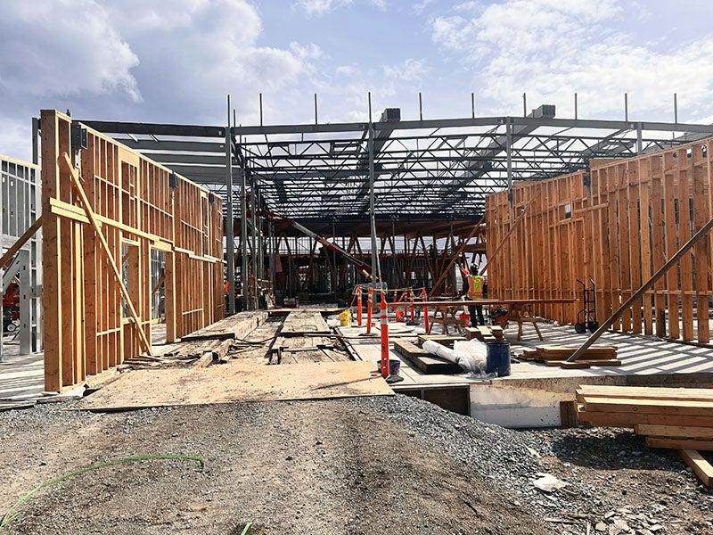 a building under construction with steel truss being installed for the roof and some wood wall framing in place