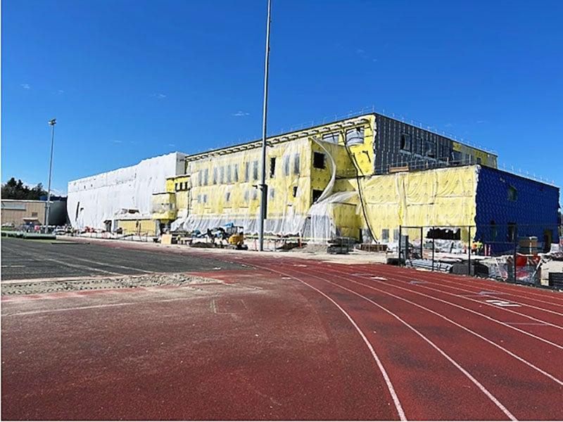 a building under construction has yellow material and plastic on it. a red track is in front.